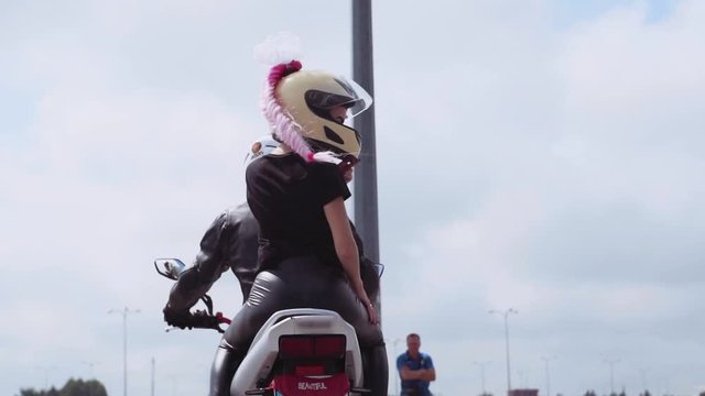 Wonderful young Caucasian woman and boyfriend riding motorcycle. Attractive Slavic girl in helmet tourning around, looking at camera.