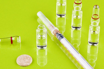 Ampoule with medicine and syringe on green background
