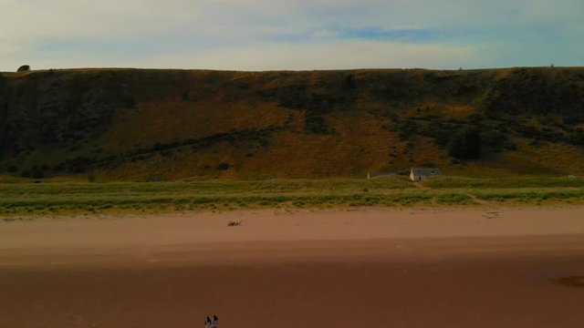 Beautiful views from drone of a long wide beach during low tide under a blue cloudy sky with some views of a family walking along.