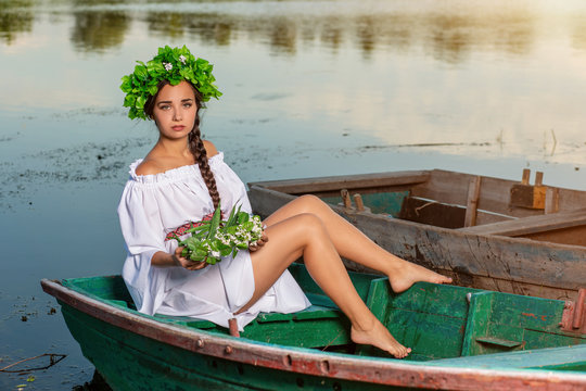 Young sexy woman on boat at sunset. The girl has a flower wreath on her head, relaxing and sailing on river. Fantasy art photography.