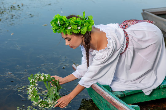 Young sexy woman on boat at sunset. The girl has a flower wreath on her head, relaxing and sailing on river. Fantasy art photography.
