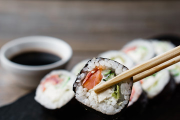 Eating sushi. Food photo art, Japanese restaurant, dinner. Pair of chopsticks taking sushi roll from tray, close up