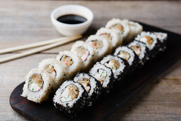 Japanese restaurant, sushi plate. Delicious seafood maki rolls on black wooden tray with sauce and chopsticks