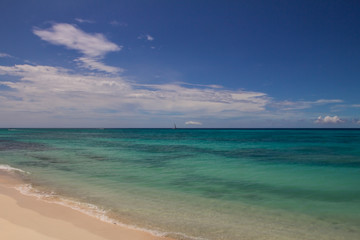 Fototapeta na wymiar Yacht on the horizon between a green ocean and the blue sky