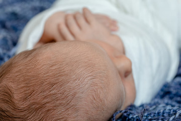 Newborn - baby, face close-up. The sleeping Newborn boy under a white knitted blanket lies on the blue fur.