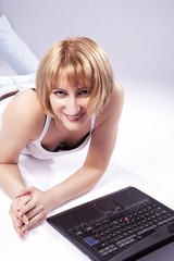 Youth Lifestyle Ideas and Concepts. Cute Caucasian Blond Woman Posing With Laptop Against White Backgound. Laying on Floor