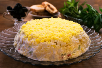 Salad with yellow top layer of egg yolks on a glass plate, basil leaves, toast, black olives.