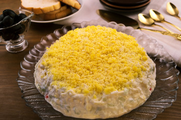 Appetizer with a bright yellow coat for the holiday table cutlery, burnt toast, black olives on a wooden background.