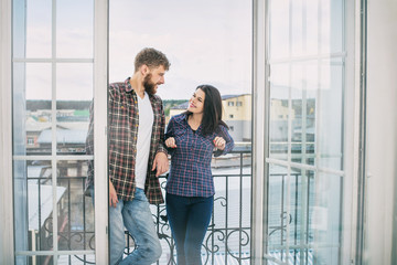 Young beautiful and happy couple man and woman at home on the balcony smiling and hugging on the background of city roofs