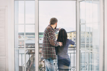 Young beautiful and happy couple man and woman at home on the balcony smiling and hugging on the background of city roofs