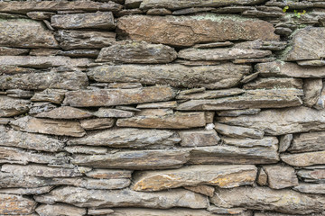 A stone wall textured pattern like bricks one over another the rocks fits perfect onto their space where in between some flora begin to grow. Wall of a town on Chilean countryside, Cobquecura, Chile