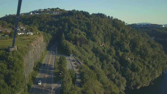 Reveal aerial shot of suspension bridge with very close flight near the column of the bridge. Weather is sunny, there are cars leaving the tuneel and entering the bridge.