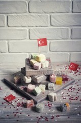 various national Oriental sweets, with paper flags of Turkey, Turkish delight on a wooden white brushed stand and on a white brushed background, vertical, the concept of the independence day of Turkey