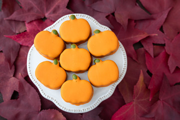 White platter with small orange frosted pumpkin cakes on background of red fall leaves
