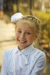 A beautiful girl with a white bow on her head laughs cheerfully before going to school.