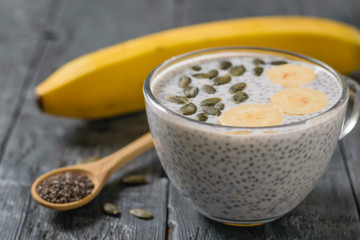 Chia seed pudding with banana and pumpkin seed on a dark wooden table.