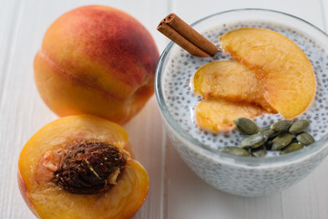 Chia seed pudding with peach and pumpkin seed and cinnamon on a white wooden table.