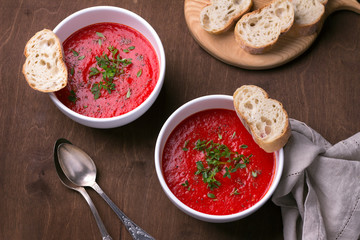 Delicious vegan soup of baked tomatoes and sweet peppers with herbs in a white plate on a wooden background, top view, horizontal