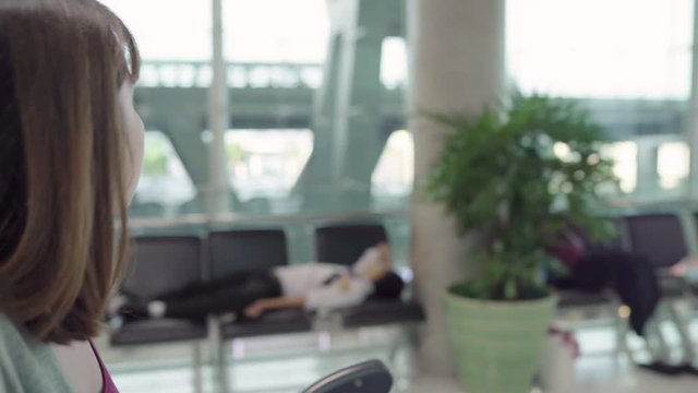 Attractive casual happy young Asian female passenger in international airport using trolley or cart with many luggage walking in terminal hall while going to boarding flight at the departure gate.