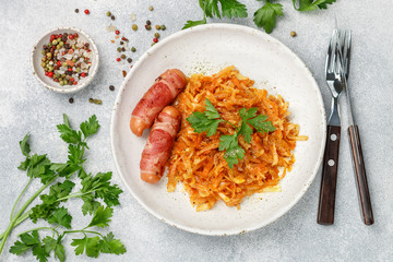 Stewed cabbage with carrots, onions and tomatoes and sausages in bacon with parsley and spices in a white plate. Bigos. Delicious lunch