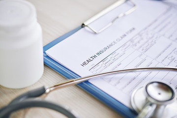 Health insurance claim form, stethoscope and container with pills on table of doctor