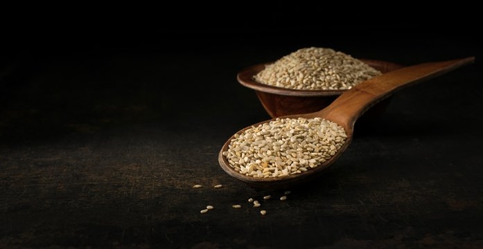 A low light image of a wooden spoon and bowl of sesame seeds with copy space for your text