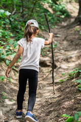 Young traveller. Small girl with wooden stick climbing in the forest.
