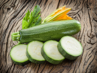 Zucchini and zucchini slice with flower and leaf on wooden background.