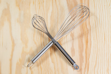 Two crossed silver whisks on a wooden table 