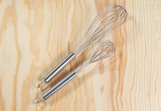 Two silver whisks lying on a wooden table 