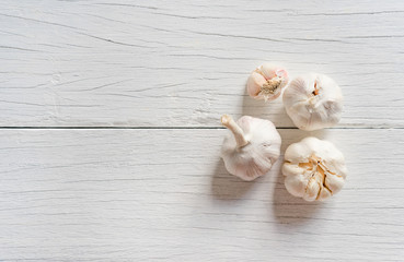 Organic garlic whole and cloves on white wood background.