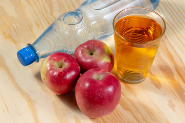 Glass of apple spritzer beside water bottle and a group of red apples on wooden table