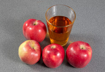 Top view on a glass of apple juice beside a group of red ripe apples