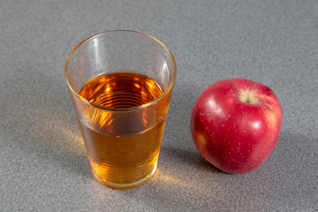 Glass of apple juice beside a red ripe apple on a grey table 