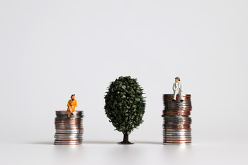 Miniature old couple sitting on a pile of coins on the both side of a tree.