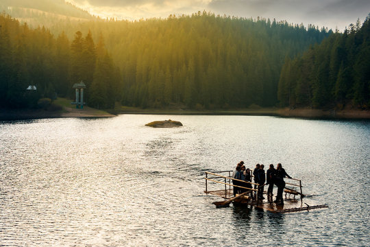 Synevir, Ukraine - OCT 20, 2008: group of young tourists on a wooden raft in the middle of a lake. gorgeous evening light above the forest on hill in the distance. wonderful atmosphere of autumn