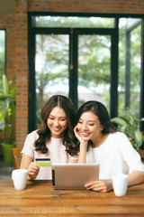 Happy relaxed young female friends doing online shopping through laptop and credit card in living room