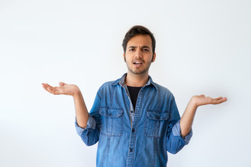 Annoyed young Indian man spreading hands in irritation. Handsome dark haired man wearing denim...