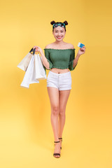 Full length portrait of a cheerful attractive woman holds shopping bags and a credit card on yellow background