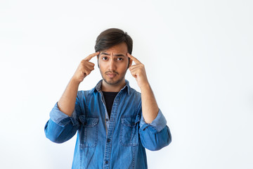 Serious young Indian man touching temples with fingers and looking at camera. Portrait of tense handsome dark haired man in denim shirt asking to think before doing. Need to think concept.