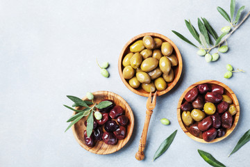 Olives in wooden bowls decorated with fresh olive tree branch top view.