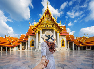 Women tourists holding man's hand and leading him to Wat Benchamabophit or the Marble Temple in Bangkok, Thailand. - obrazy, fototapety, plakaty