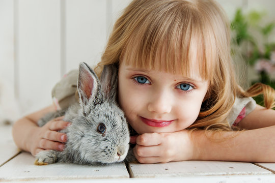 Cute girl hugging with rabbit while lying on the floor at home