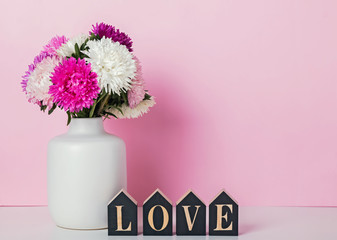 Pink and white flowers in thevase and wooden letters arranged in a word Love