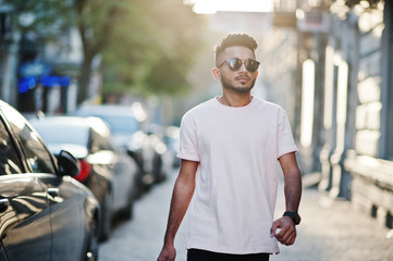 Stylish indian beard man at sunglasses and pink t-shirt. India model walking outdoor sunset at...
