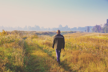 A man walking along a country road through the field early in the morning - Powered by Adobe