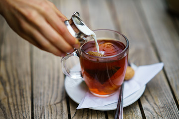 Pouring milk in tea in glass cup on wooden table