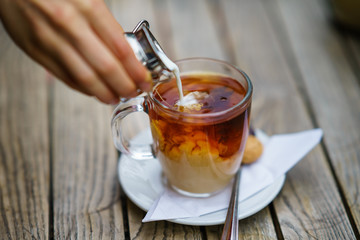 Pouring milk in tea in glass cup on wooden table