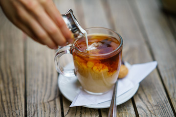 Pouring milk in tea in glass cup on wooden table