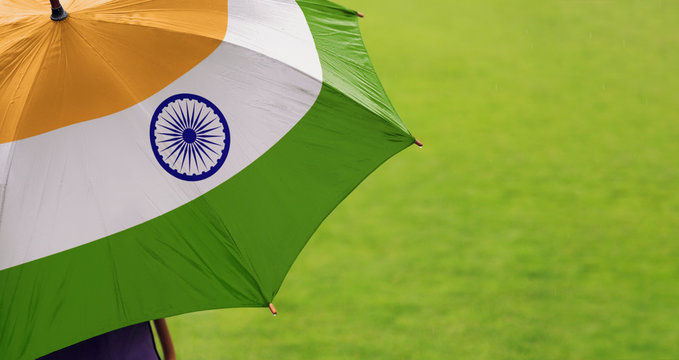 India flag umbrella. Close up of printed umbrella over green grass lawn / field. Rainy weather forecast concept.	